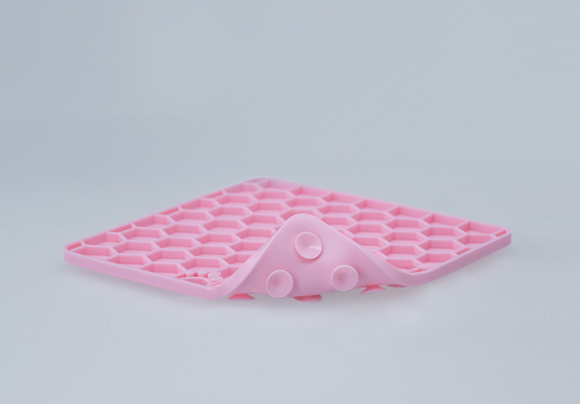 Pink silicone honeycomb lick mat flexed to show its pliable construction