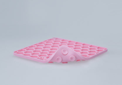 Pink silicone honeycomb lick mat flexed to show its pliable construction